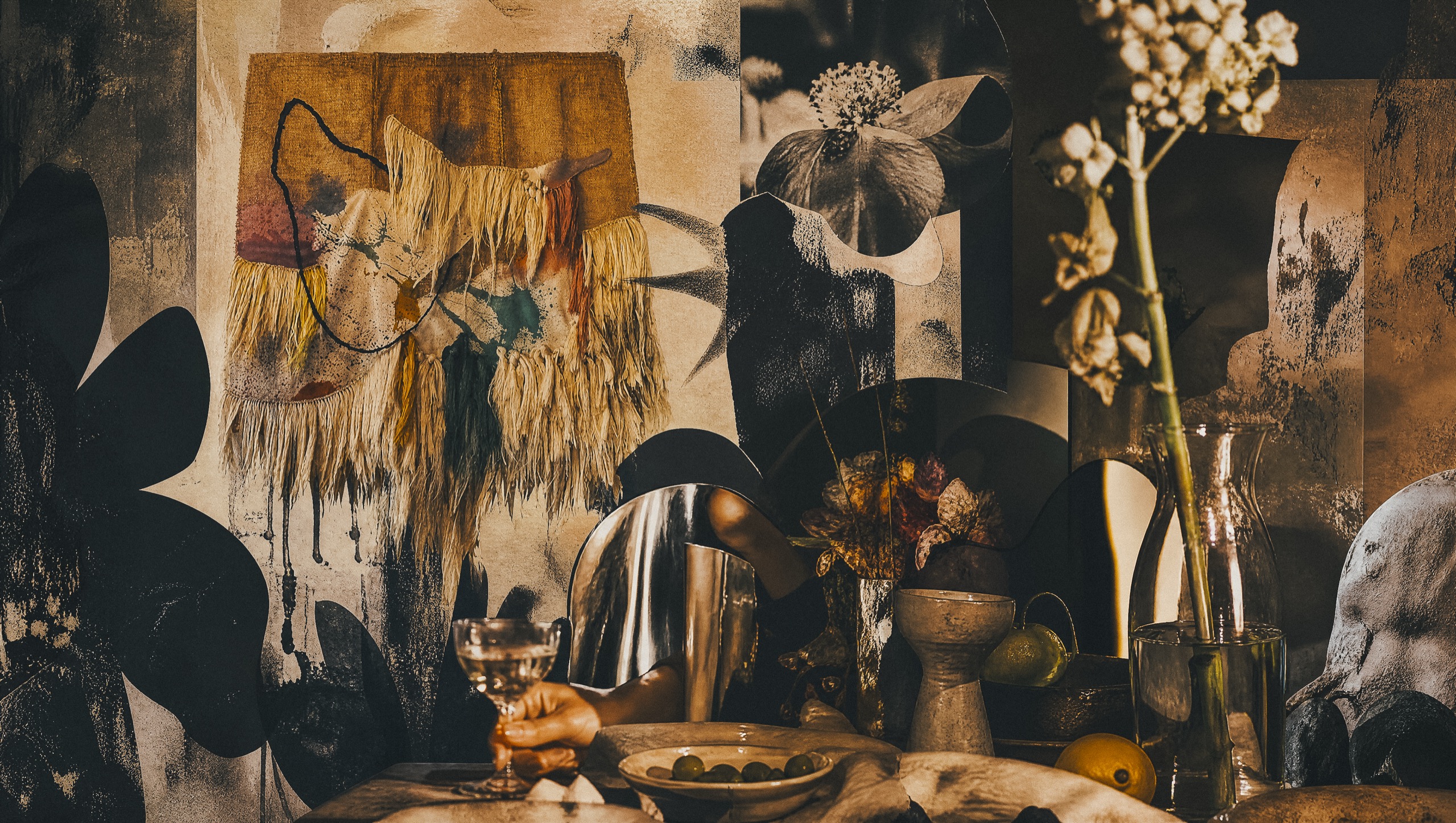 A dark, textured still life of a set table with dried flowers, ceramics and a glass of wine