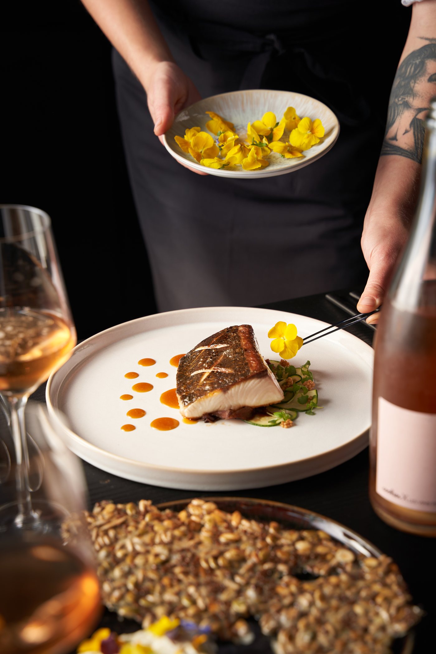 A plated fish course finished with yellow edible flowers
