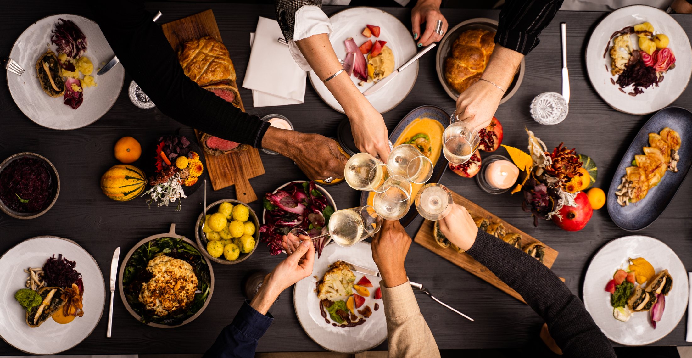 Hands raising glasses over a long table full of food